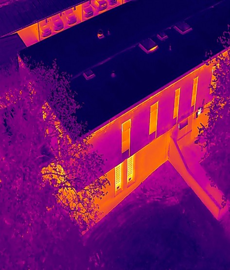 Handheld FLIR thermal camera surveying an office inside Bridgnorth Police Station, with the thermal display showing heat distribution across the wall